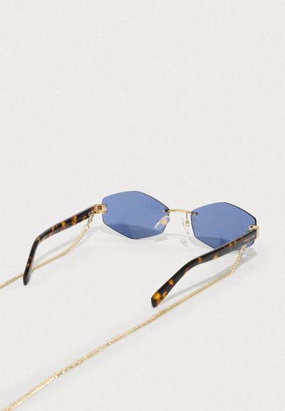 Εξάγωνες ηλιόφως με μπλε φακούς, βραχίονες με καχεκτικό σχέδιο και χρυσές αλυσίδες. Διαφανείς υποστηρικτές μύτης ασφαλίζουν το πλαίσιο.