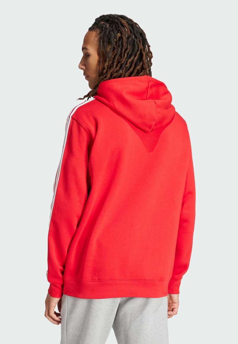 Sweatshirt à capuche rouge avec des rayures blanches sur les côtés, fabriqué en tissu doux. Présente une coupe décontractée et des poignets côtelés.