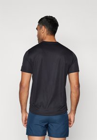 Crni kratki rukavi T-shirt izrađen od glatkog materijala, s okruglim izrezom i opuštenim krojem, uparen s tamnoplavim šortsevima.