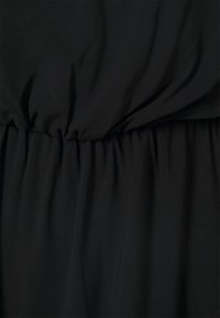 Tecido preto com uma cintura elástica franzida. Textura suave com um caimento leve e brilho sutil, criando uma silhueta descontraída.