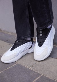 Zapatillas deportivas en blanco y negro con un diseño texturizado, fabricadas con materiales de malla y ante, que presentan acentos en forma de cono y una suela acolchada.