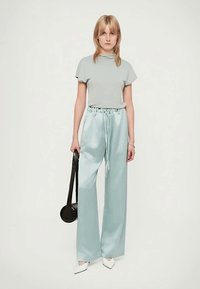 Ανοιχτό γκρι εφαρμοστό τοπ με κοντά μανίκια, συνδυασμένο με σατέν παντελόνες ψηλόμεσες με φαρδιά μπότα σε απαλό γαλάζιο. Το μοντέλο κρατάει μια στρογγυλή μαύρη τσάντα.