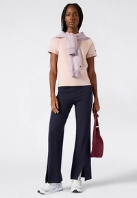 Różowy t-shirt z krótkim rękawem z logo, narzucony liliowy sweter, granatowe spodnie o szerokich nogawkach z rozcięciami, białe trampki i bordowa torba.