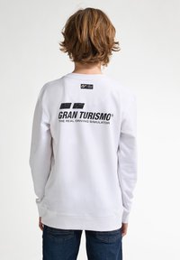 Sudadera blanca de manga larga, con cuello redondo. Texto negro "GRAN TURISMO" y eslogan en la parte posterior, textura de algodón suave.