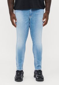 Light blue skinny jeans made of denim with a faded finish. Worn with black athletic shoes featuring purple accents and a textured design.
