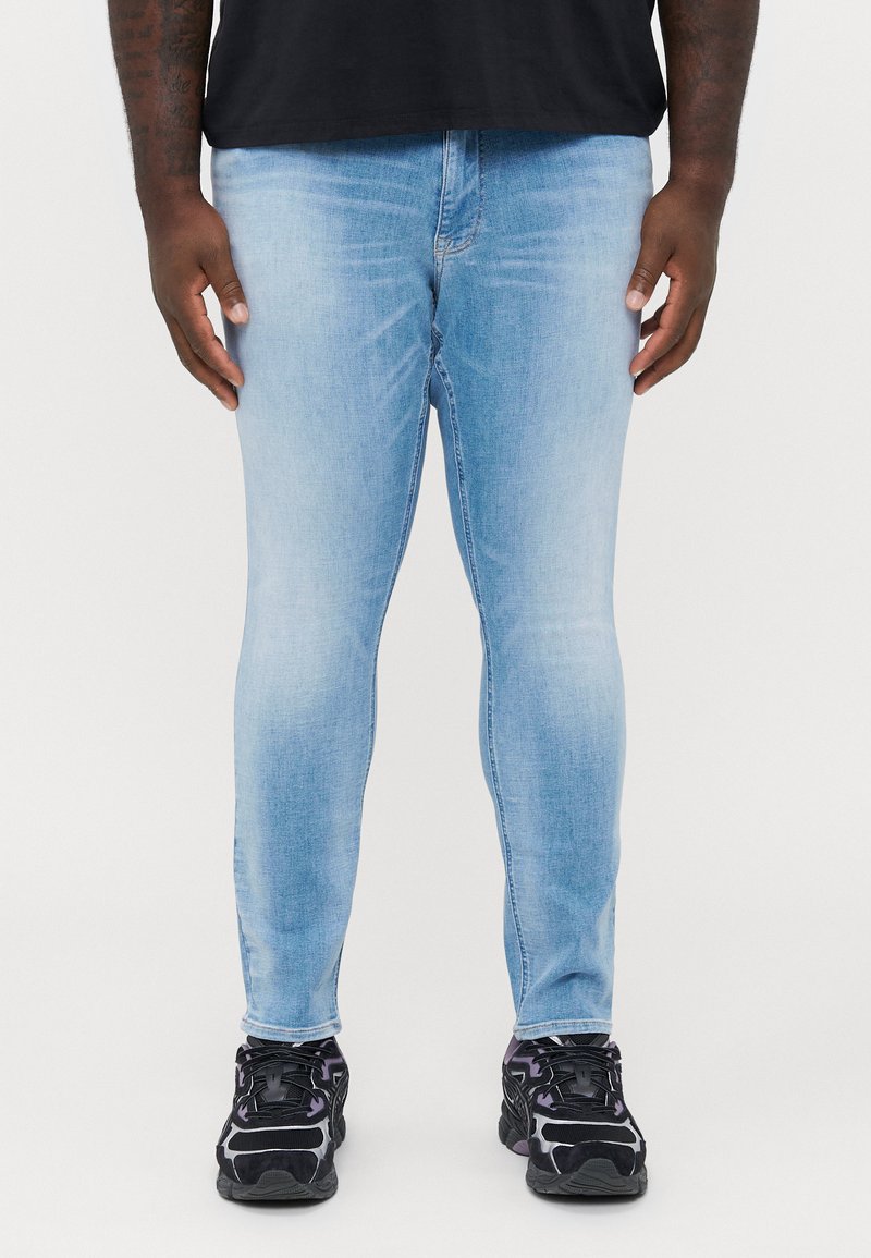 Light blue skinny jeans made of denim with a faded finish. Worn with black athletic shoes featuring purple accents and a textured design.