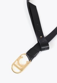 Svart läderbälte med spänne i guldmetall som har en cirkelformad urholkning. Slät textur med justerbara hack på remmen.
