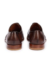 Scarpe in pelle marrone con una texture liscia, forma arrotondata, dettagli di cucitura minimi e una suola in legno a contrasto. Presentano accenti rossi sottili.