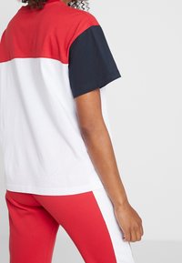 Camiseta en bloques de color rojo, azul marino y blanco, con mangas cortas y un corte relajado. Material de algodón con una textura suave. Diseño sencillo.