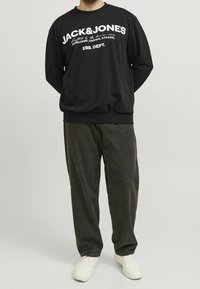 Felpa nera con logo in testo bianco, collo rotondo, maniche lunghe e polsini a coste. Abbinata a pantaloni scuri e larghi e sneakers bianche.
