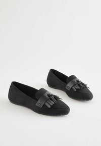 Sorte ruskind loafers med flad sål, der har en frynse-accent foran og et kontrasterende læderbånd. Glat tekstur, minimalistisk design.