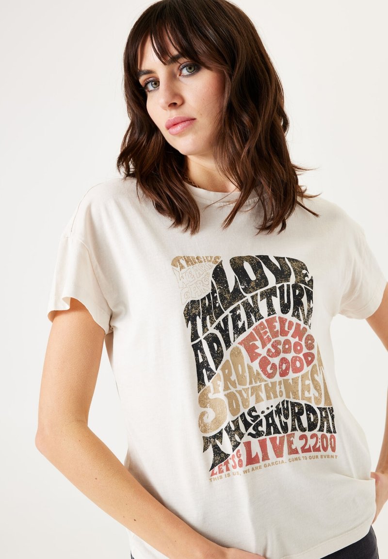 Camiseta de algodón crema con mangas cortas, que presenta una tipografía en negrita y texturizada en negro, dorado y rojo, centrada en el frente.