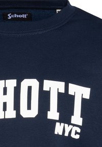 Marineblauwe t-shirt van katoen, met grote witte tekst die "SCHOTT NYC" zegt. Crew neck ontwerp met geribbeerde textuur.