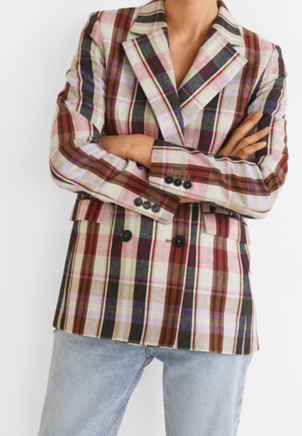 Personne portant un blazer croisé à carreaux avec des rayures marron, rouge, noir et blanc, bras croisés, associé à un jean bleu clair.