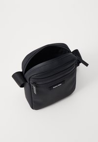 Borsa a tracolla nera con scomparti con zip, realizzata in materiale liscio e rete testurizzata. Dotata di tracolla regolabile e logo Calvin Klein.