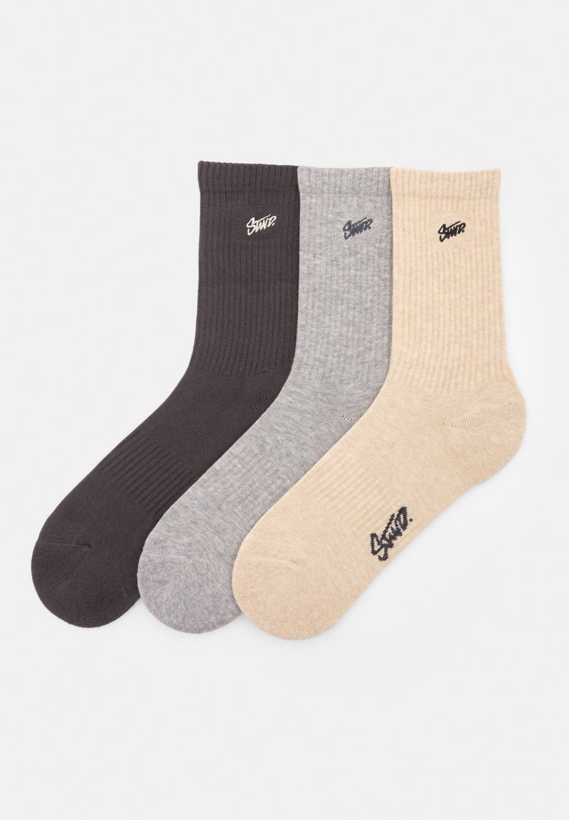 Tre par ribbede sokker i mørkegrå, lys grå og beige, hver med et lille broderet logo.