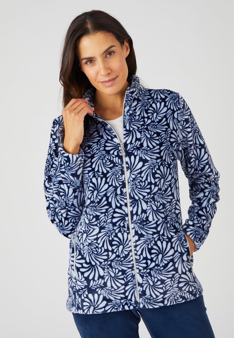 Giacca di pile con sfondo blu navy, caratterizzata da un motivo floreale bianco. Ha un colletto alto, zip frontale e tasche laterali.