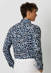 Langärmliges Hemd mit einem marineblauen und weißen geometrischen Muster, aus leichtem Stoff mit Kragen und Knopfdetails auf der Rückseite.