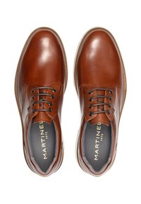 Zapatos de vestir de cuero marrón con textura suave, punta redondeada y cierre de cordones. Presentan un forro gris y un logotipo sutil en la plantilla.