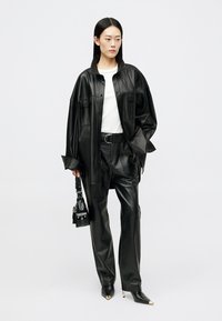 Μαύρο δερμάτινο πουκάμισο και παντελόνι, άσπρο t-shirt από κάτω, σετ με μικρή μαύρη τσάντα και γόβες με μυτερή μύτη. Λείο υλικό, άνετη εφαρμογή.