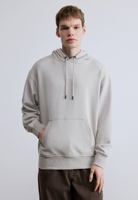 Helehall kapuutsiga dressipluus kängurutasku ja nööriga kapuutsiga. Esiküljel on peen toon-toonis logoga ning varrukatel ja äärel soonikkoes mansetid.