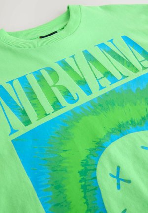T-shirt en coton vert avec un grand graphique bleu et vert représentant le mot "NIRVANA" et un visage souriant avec des yeux en X et un design circulaire.