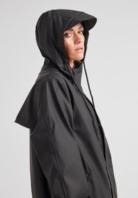 Svart vattentät jacka med huva, med en snygg, minimalistisk design, justerbara dragsko och en något oversized passform.