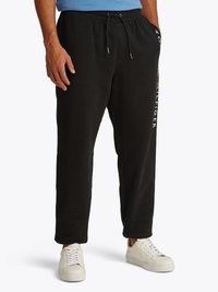 Pantaloni sportivi neri con vita regolabile, tasche laterali e testo bianco sulla gamba sinistra. Abbinati a scarpe da ginnastica bianche e una maglietta blu.
