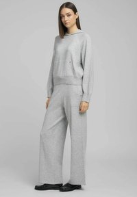 Sudadera gris de mezcla de algodón con bolsillo frontal, combinada con pantalones anchos a juego. El conjunto presenta un ajuste relajado y puños acanalados.