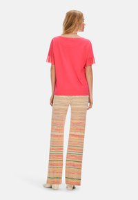 Coral short-sleeve top with fringed sleeves paired with patterned beige wide-leg pants featuring colorful zigzag designs and cream-colored shoes.