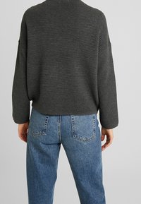 Grauer gerippter Pullover mit lockerer Passform und abgesenkten Schultern, kombiniert mit hochgeschnittenen blauen Jeans aus Denim, die eine leichte Waschung und Taschen-Design aufweisen.