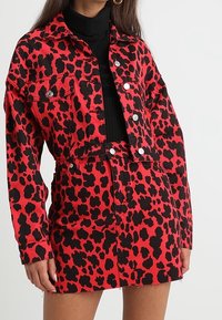 Röd och svart leopardmönstrad denimjacka med matchande kjol, som har en kort design, framknappar och två sidfickor.
