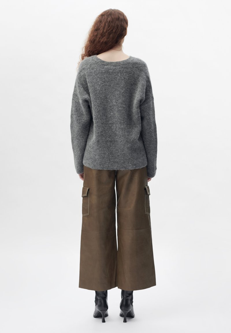 Grauer Strickpullover mit lockerer Passform, kombiniert mit weiten braunen Leder-Cargohosen, die seitliche Taschen und Kontrastnähte aufweisen.