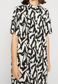 Schwarz-weiß gemustertes kurzärmeliges Hemdkleid mit Knopfleiste und Kragen, aus fließendem Stoff.