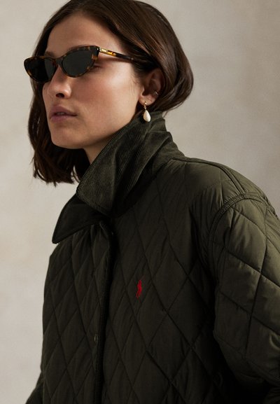 Naine kannab tumeda kilpkonnamustriga kassisilu päikeseprille, pärlitilk kõrvarõngast ja tikkimismustriga tumerohelist jope, millel on kõrge krae.