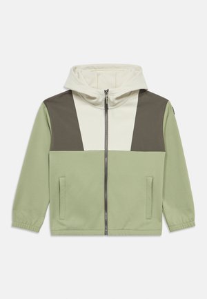 Veste zippée verte avec capuche, présentant un motif géométrique blanc et marron foncé sur le haut du devant, tissu texturé et poches latérales.