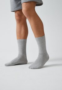 Graue Baumwollsocken mit gerippter Textur, knöchellang und mit glatter Oberfläche. An den Füßen einer Person präsentiert, kombiniert mit grauen Shorts.