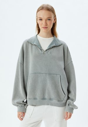 Grauer übergroßer Sweatshirt aus weichem Stoff, mit Kragen, gerippten Bündchen und einer Fronttasche. Glatte Textur und entspannte Passform.