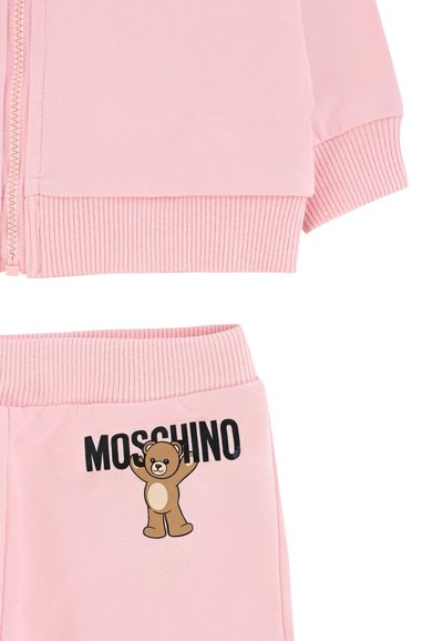 Rosa zip-up jakke med ribbede manchetter, parret med matchende bukser, der har et bjørnegraphic og "Moschino" logo i sort. Blød stoftekstur.
