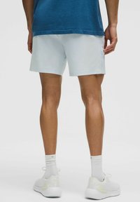 Lyseblå træningsshorts lavet af et glat stof, med et simpelt design og en komfortabel pasform, iført med hvide sko og sokker.