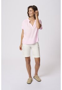 Chemise à col rose à manches courtes avec une coupe décontractée, associée à un short blanc jusqu'aux genoux et des chaussures à enfiler beiges. Texture de tissu lisse.