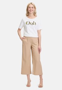 T-shirt blanc à manches courtes avec imprimé "Ooh" en motif animal, associé à un pantalon large beige. Tissu doux, coupe décontractée.