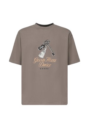 Camiseta marrón de manga corta con un diseño de una llave y un borlas. El texto dice "GRAND HOTEL DRÔLE" en naranja. Cuello redondo.