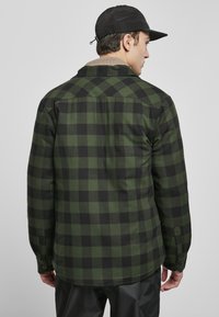 Zielona i czarna koszula flanelowa w kratę, z kołnierzykiem zapinanym na guziki, długimi rękawami i zaokrąglonym dołem, wyświetlona z tyłu.