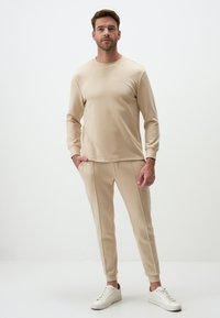 Beige sweatshirt and matching tapered joggers made of soft fabric, featuring long sleeves, crew neckline, and side pockets. White sneakers complete the look.