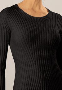 Robe noire côtelée présentant un motif vertical, un col rond et des manches longues, confectionnée dans un tissu doux et texturé.