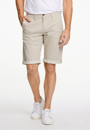 Beige, rullad ärmshorts tillverkade av ett texturerat tyg, med framfickor och knappstängning, kombinerade med vita sneakers.