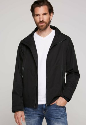 Zwarte jas van lichtgewicht materiaal, met een rits aan de voorkant, een verstelbare kap en twee zijzakken. Witte V-hals shirt eronder.