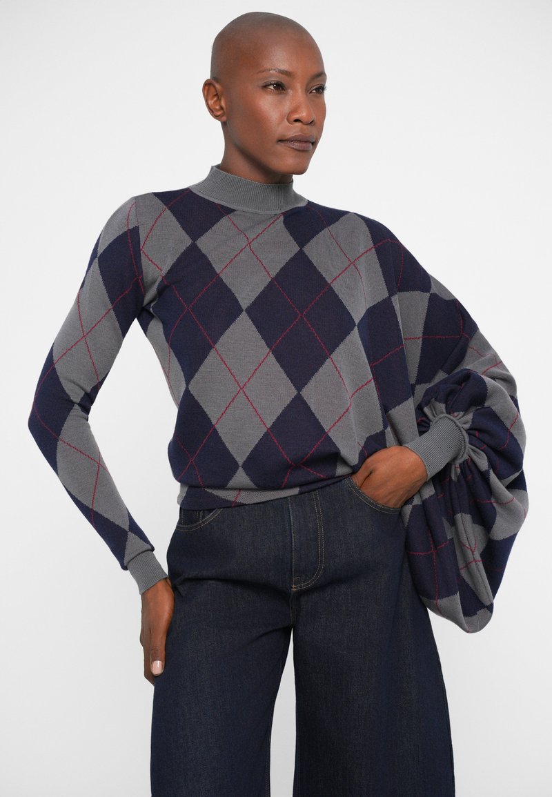 Maglione in maglia a motivo argyle grigio e navy con collo alto e maniche morbide, abbinato a jeans di denim scuri a vita alta.
