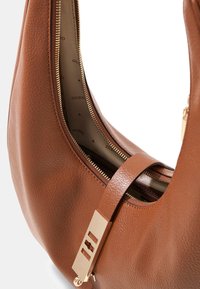 Bruine leren handtas met een gebogen vorm, ritssluiting en gouden hardware detail. Binnenin een beige voering met herhaald merklogo.